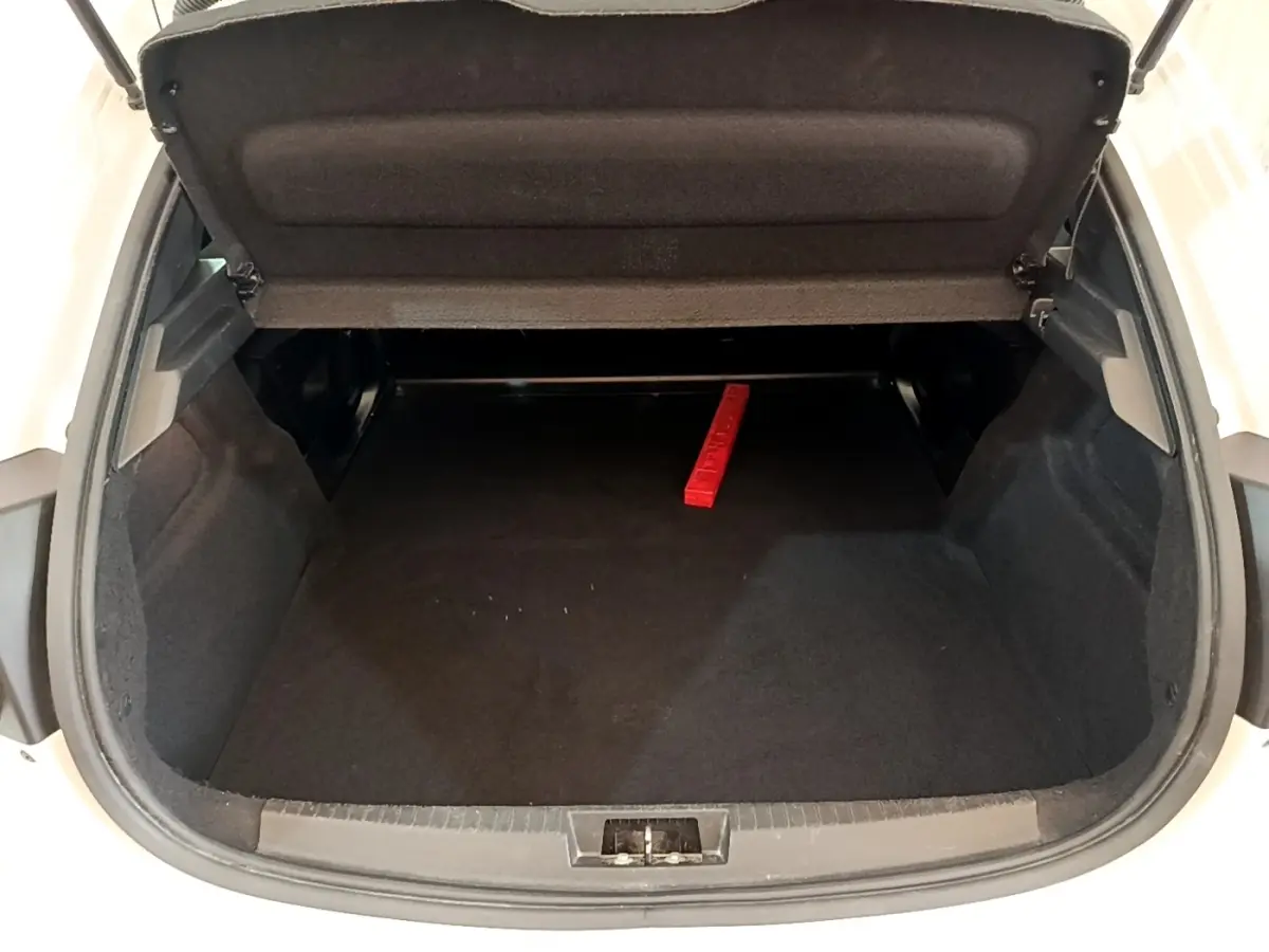 Coffre ouvert de la Peugeot 208 blanche vue de l'arrière, montrant un espace de chargement vide avec un triangle de signalisation rouge.