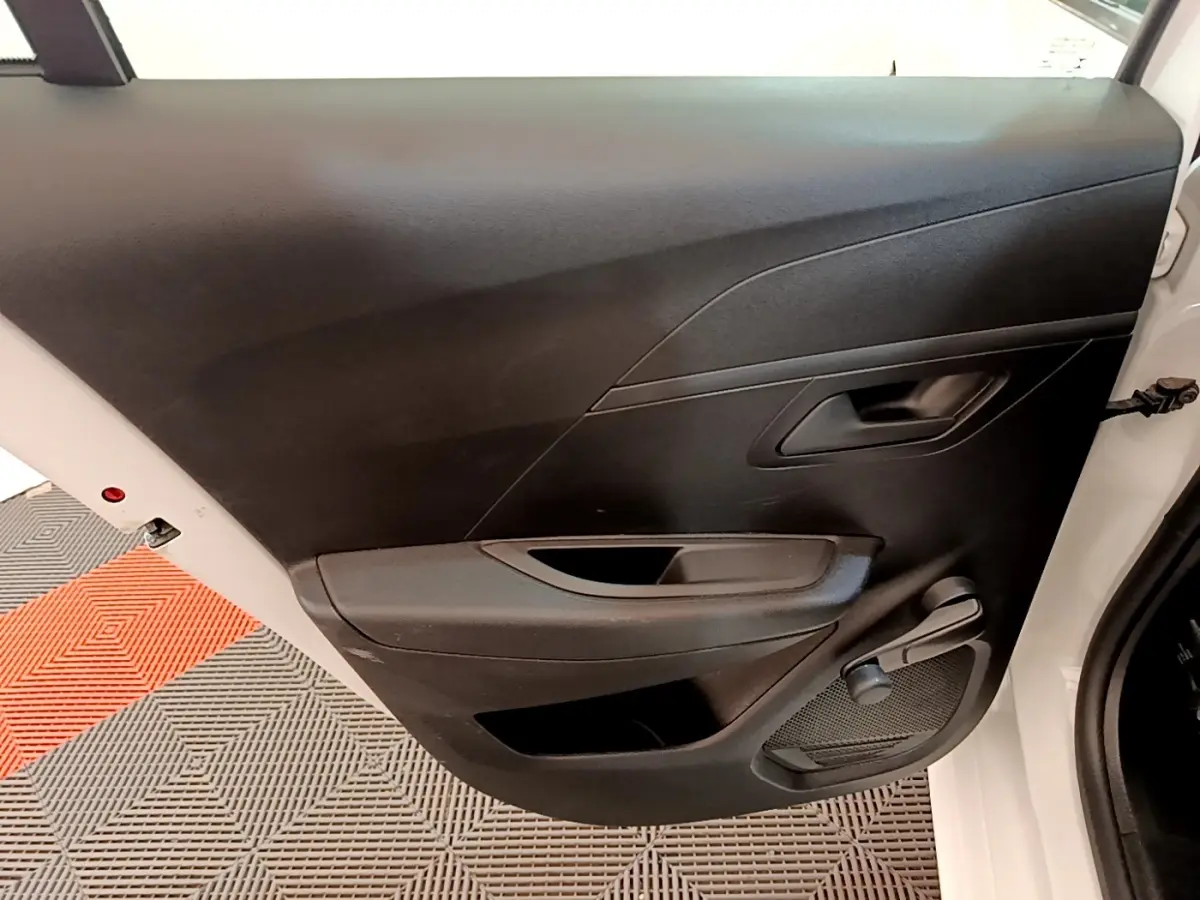 Vue rapprochée de la porte arrière droite noire d’une Peugeot 208 blanche, avec poignée et manivelle de vitre.