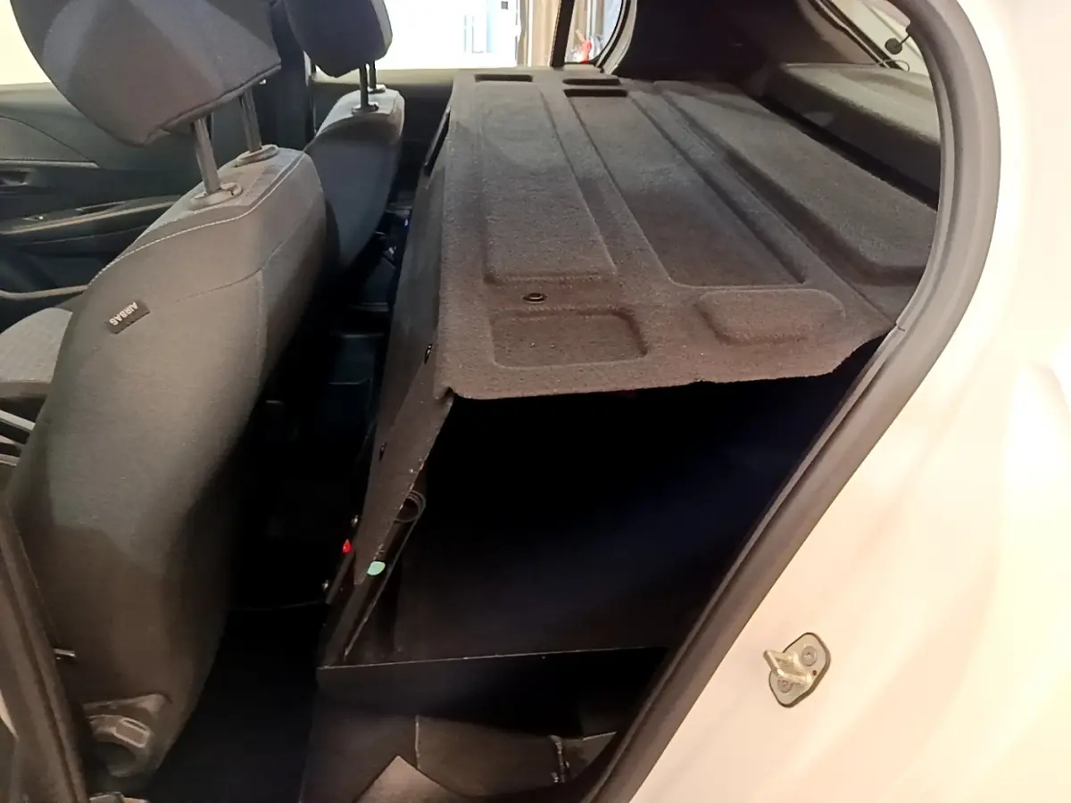 Vue intérieure arrière droite de la Peugeot 208 blanche, montrant la cloison pleine et les sièges noirs.