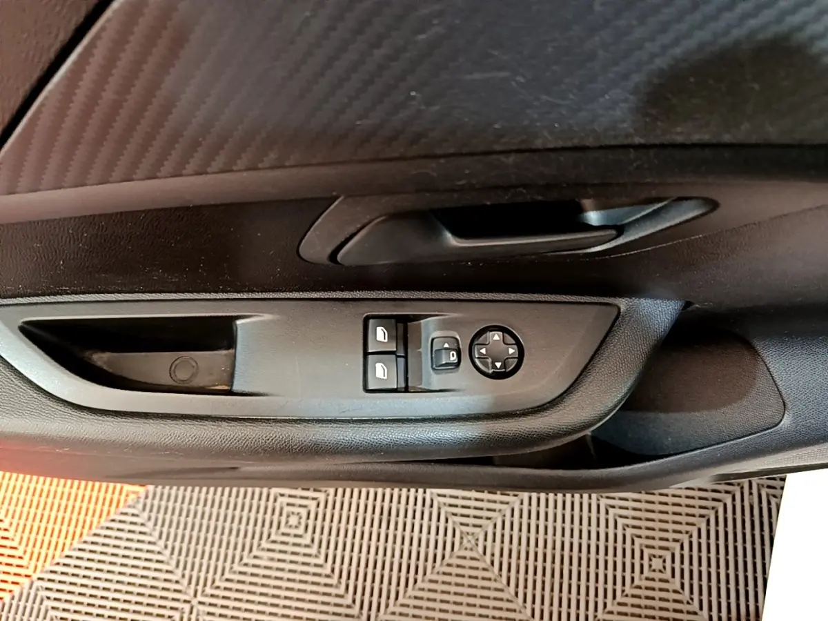 Vue rapprochée de la porte côté conducteur de la Peugeot 208 blanche, montrant les commandes des vitres et rétroviseurs.