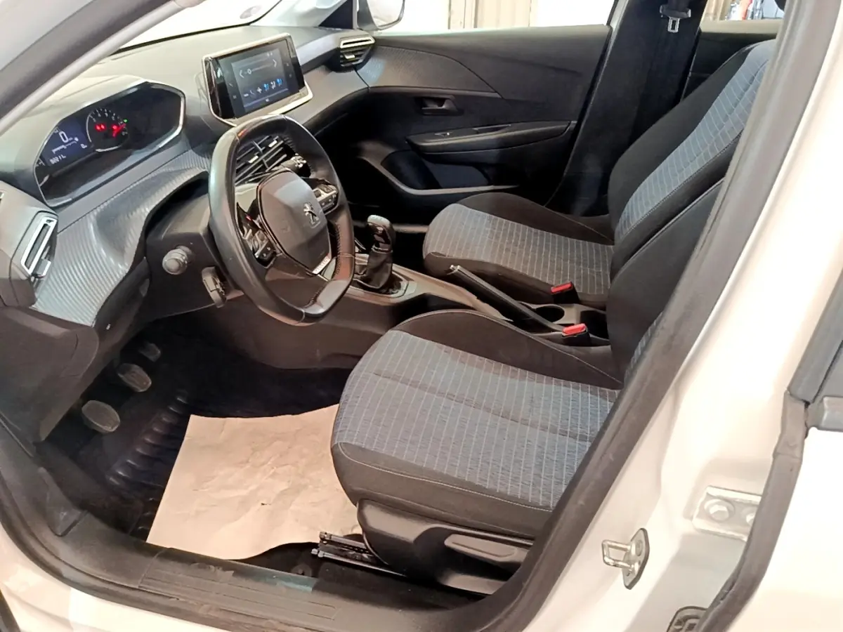 Intérieur de la Peugeot 208 blanc vue côté conducteur, montrant sièges tissu gris et tableau de bord numérique.
