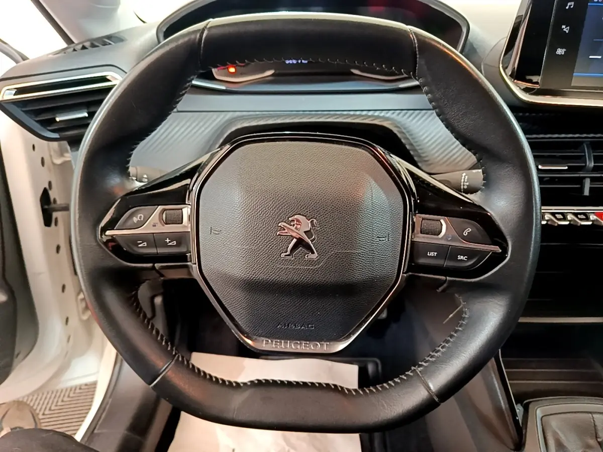 Vue rapprochée du volant noir de la Peugeot 208 blanc 2021, avec commandes intégrées et logo lion central.