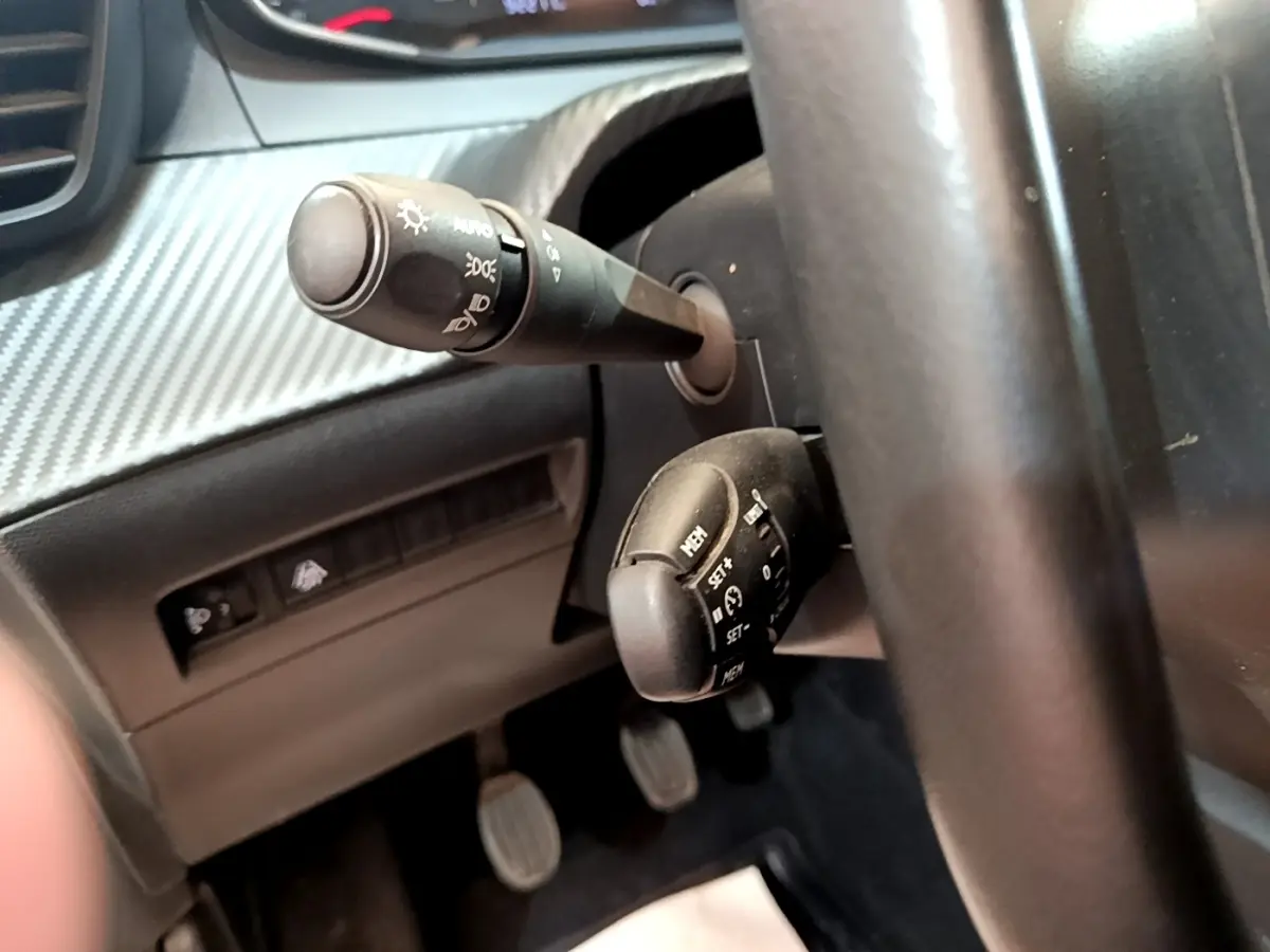 Gros plan sur la colonne de direction et commandes du volant d’une Peugeot 208 blanche, version essence 2021.