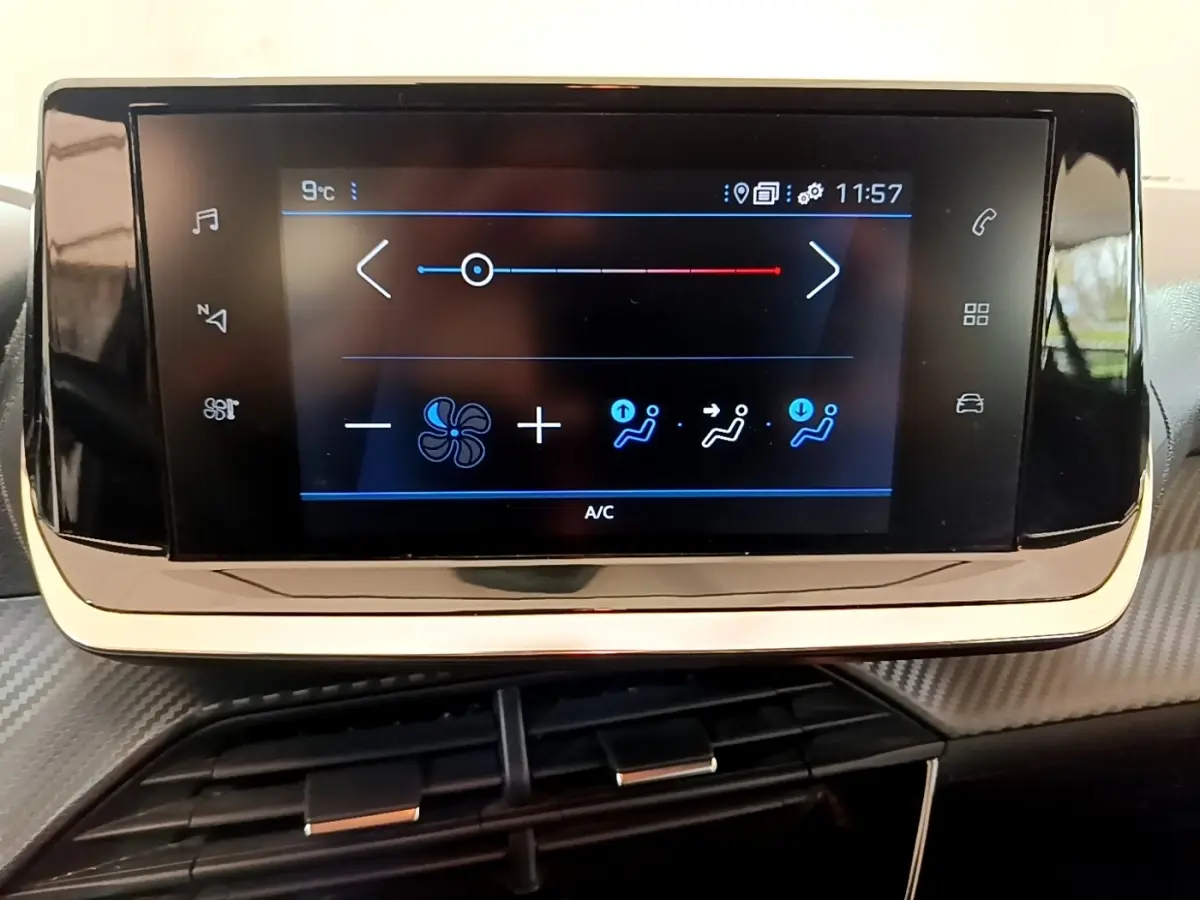 Écran tactile central noir affichant les commandes de climatisation dans l'habitacle d'une Peugeot 208 blanche.