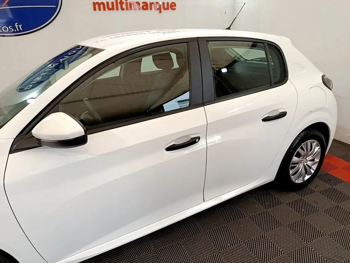 Profil côté gauche d'une Peugeot 208 blanche 2021, avec rétroviseur et poignées de porte visibles en intérieur showroom.