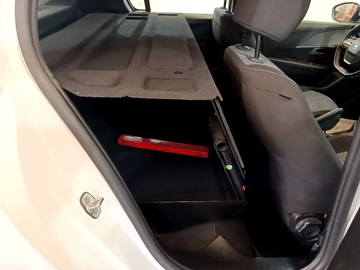 Vue intérieure côté gauche du coffre ouvert d'une Peugeot 208 blanche avec banquette arrière et siège avant en tissu gris.