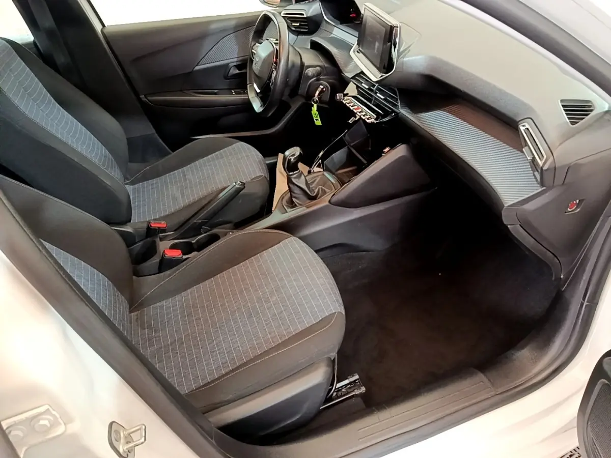 Intérieur de la Peugeot 208 blanc vue côté conducteur, montrant sièges tissu gris et tableau de bord moderne.