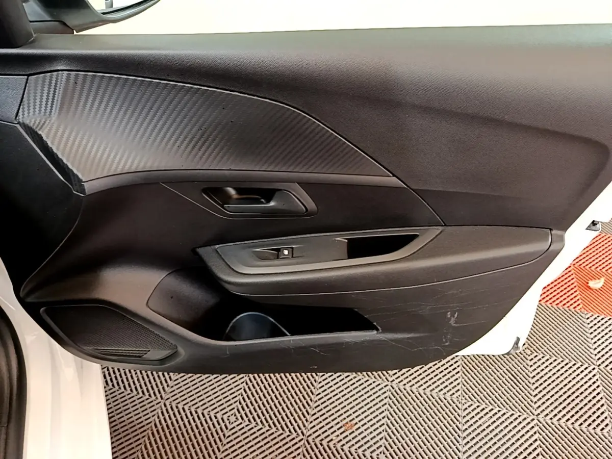 Vue intérieure de la porte avant gauche noire avec poignée et commande de vitre d'une Peugeot 208 blanche.