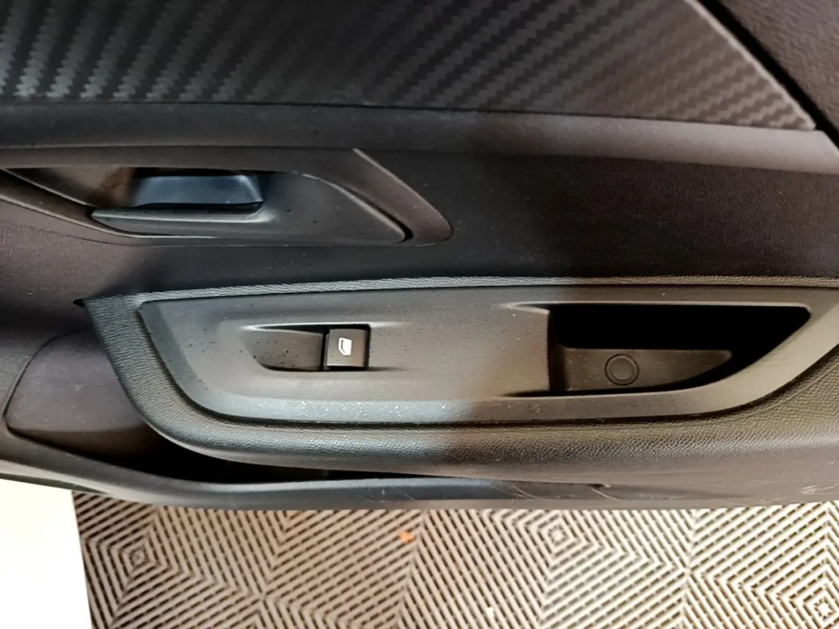 Vue rapprochée de la porte intérieure côté gauche de la Peugeot 208 blanche, avec commande de lève-vitre et poignée noire.