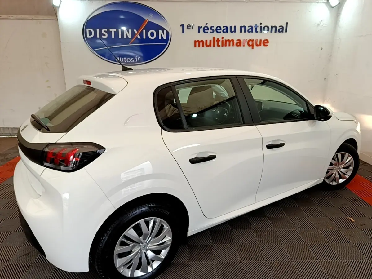 Peugeot 208 blanche vue 3/4 arrière droit en intérieur, avec feux arrière LED et jantes alliage visibles.