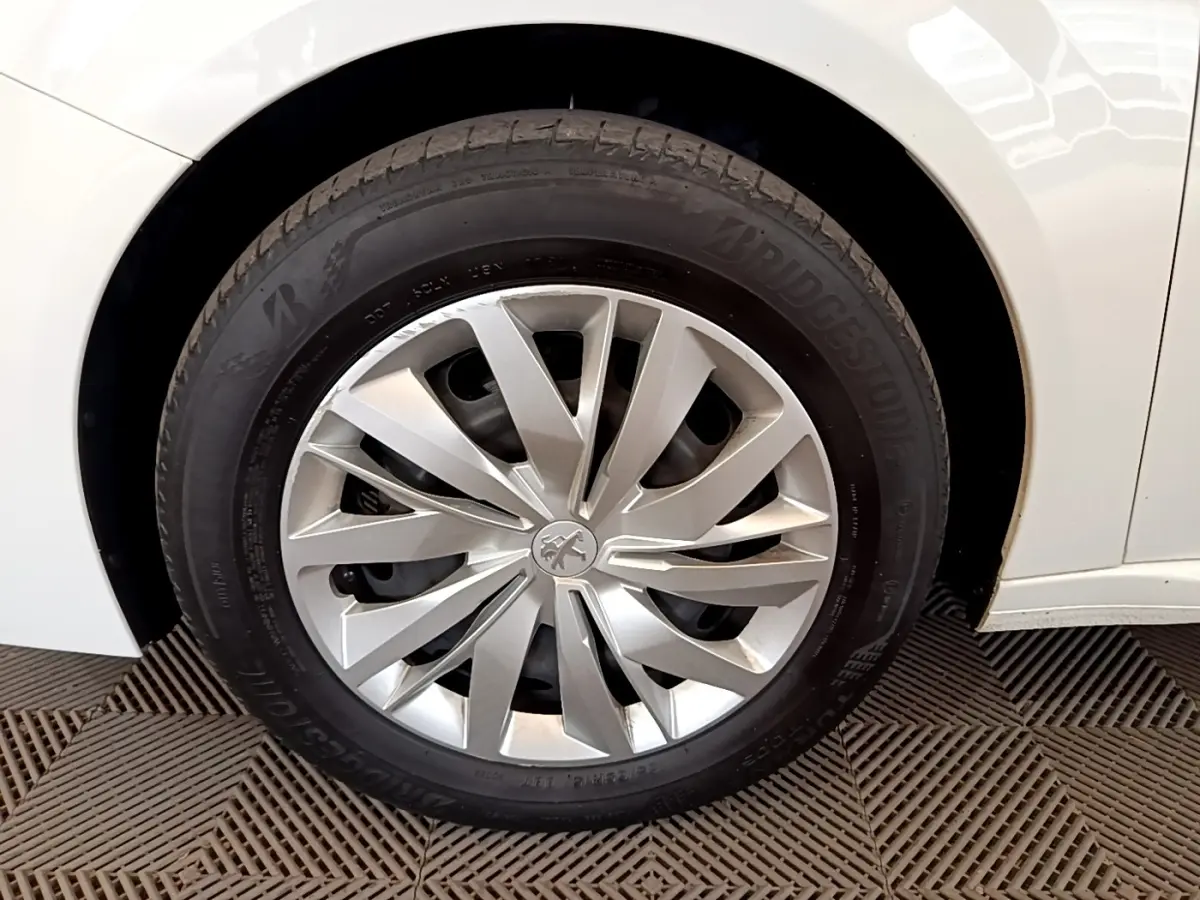 Gros plan sur la roue avant droite d'une Peugeot 208 blanche, mettant en valeur la jante argentée au design moderne.