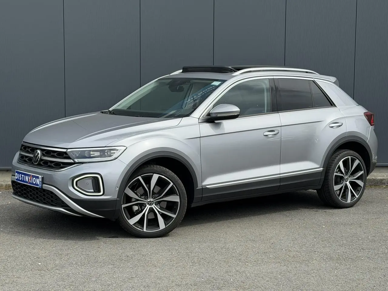 Volkswagen T-Roc argent pyrite en 3/4 avant droit, avec jantes alliage 19 pouces et toit ouvrant vitré.