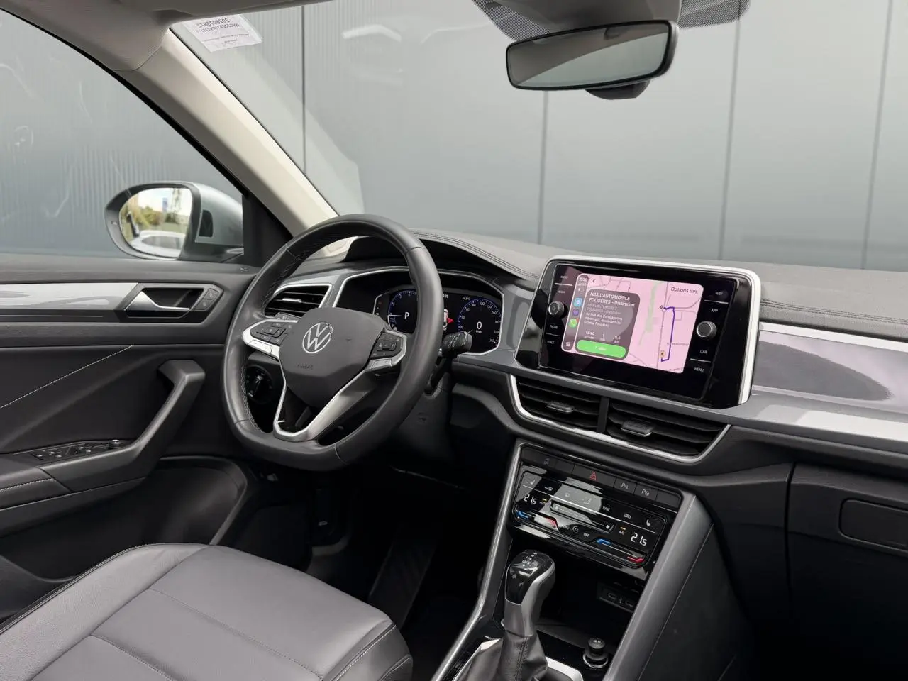 Vue intérieure côté conducteur du Volkswagen T-Roc 2024 avec tableau de bord noir et écran tactile central allumé.