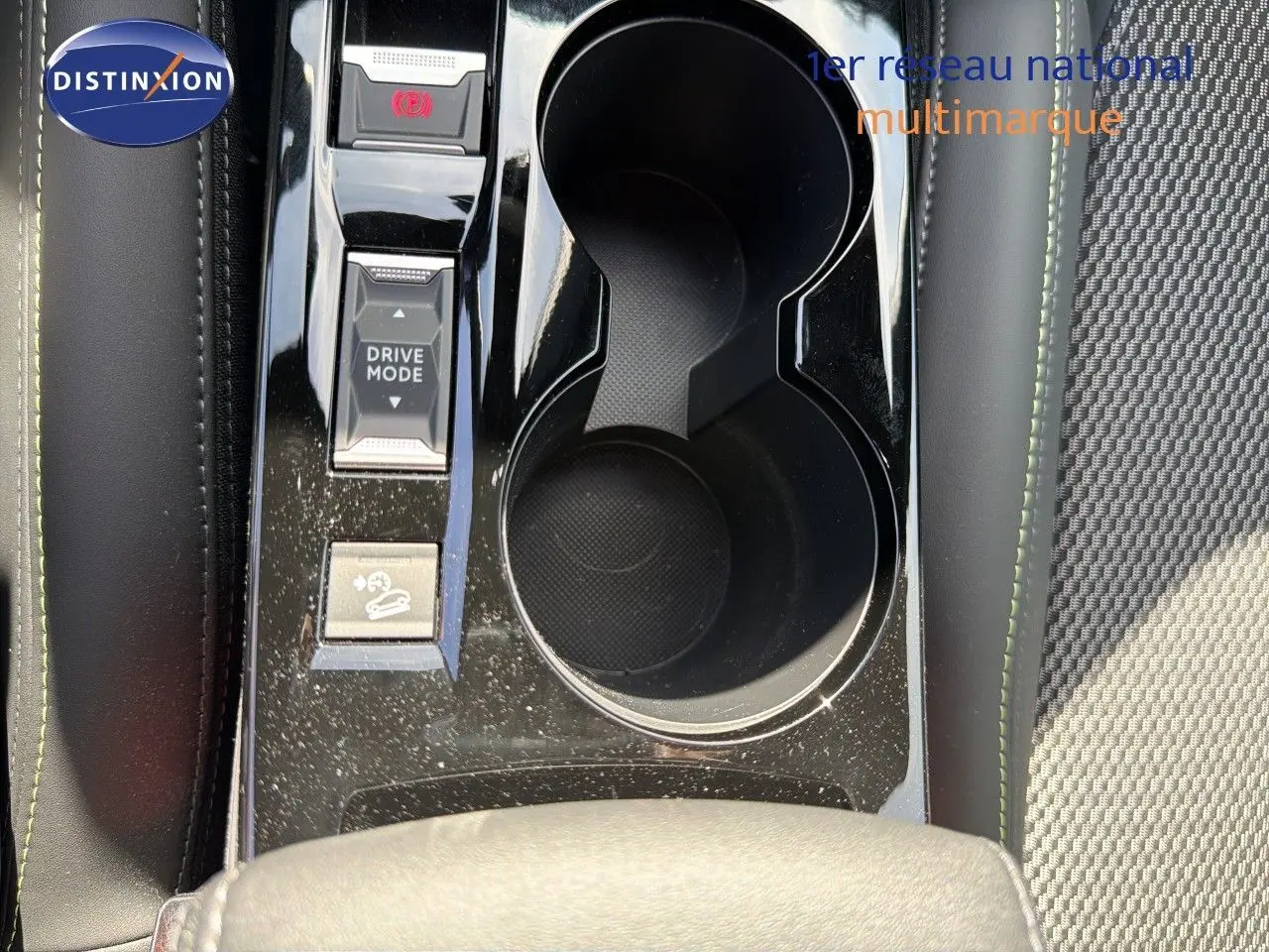 Gros plan sur la console centrale du Peugeot 2008 hybride 2026, montrant les porte-gobelets et les boutons Drive Mode.