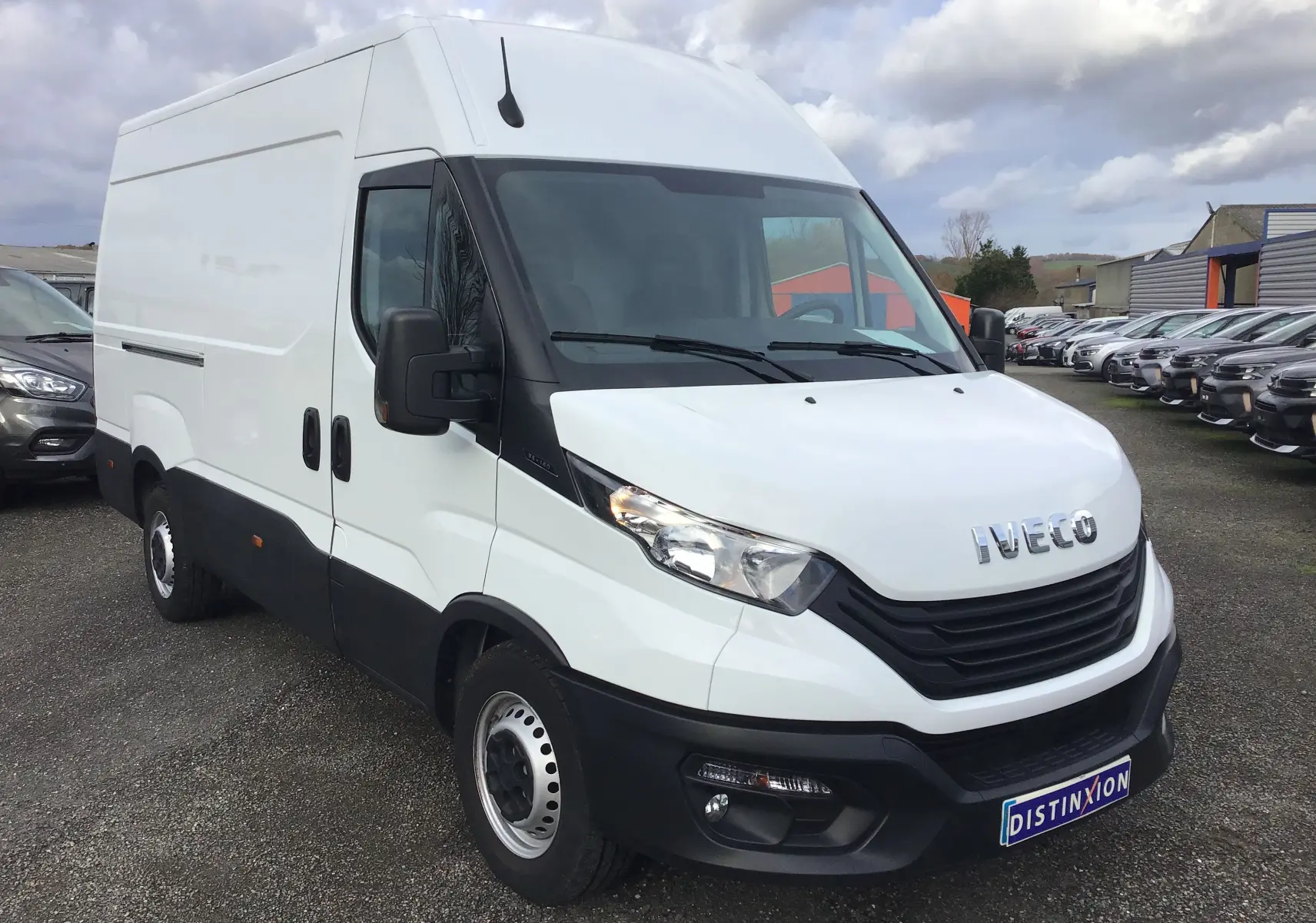 Vue 3/4 avant d'un fourgon Iveco Daily blanc avec calandre noire et rétroviseurs noirs sur parking.