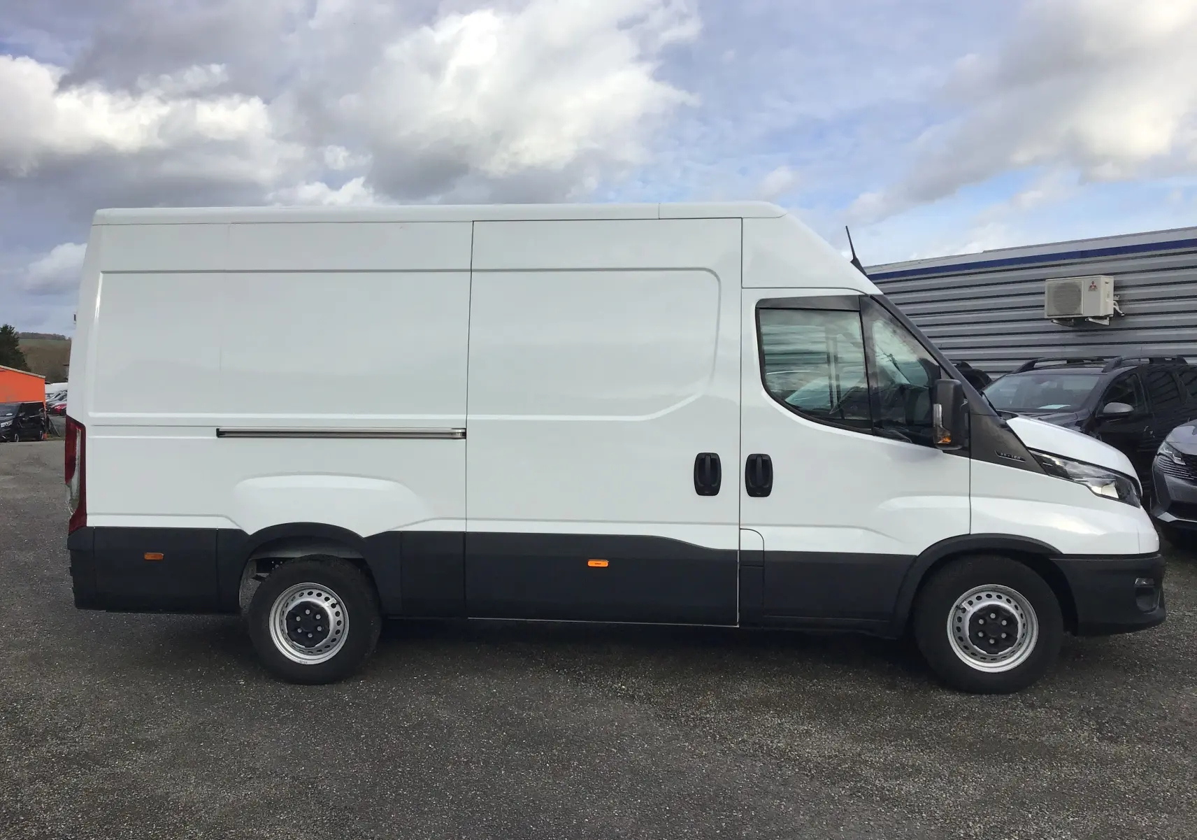 Vue de profil côté gauche d'un fourgon blanc Iveco Daily 35S16 V12 2022 avec bas de caisse noir et porte latérale double.