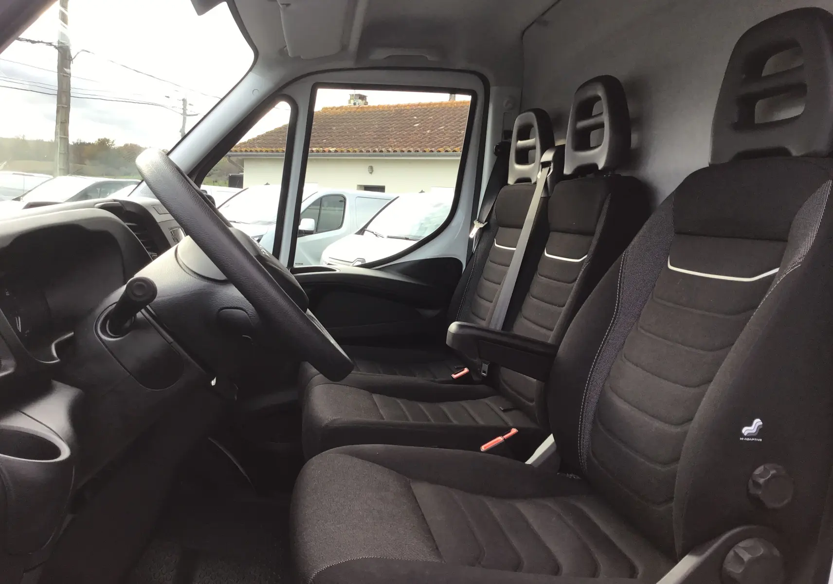 Vue intérieure côté conducteur de l'Iveco Daily Fourgon 2022 avec sièges noirs et tableau de bord gris.