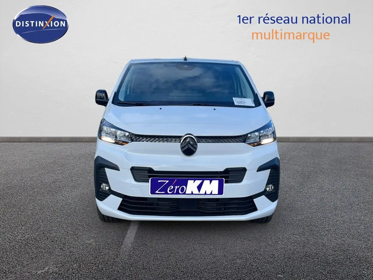 Vue frontale d'un Citroën Jumpy Fourgon XL blanc Kaolin, avec calandre noire et phares allumés sur parking.