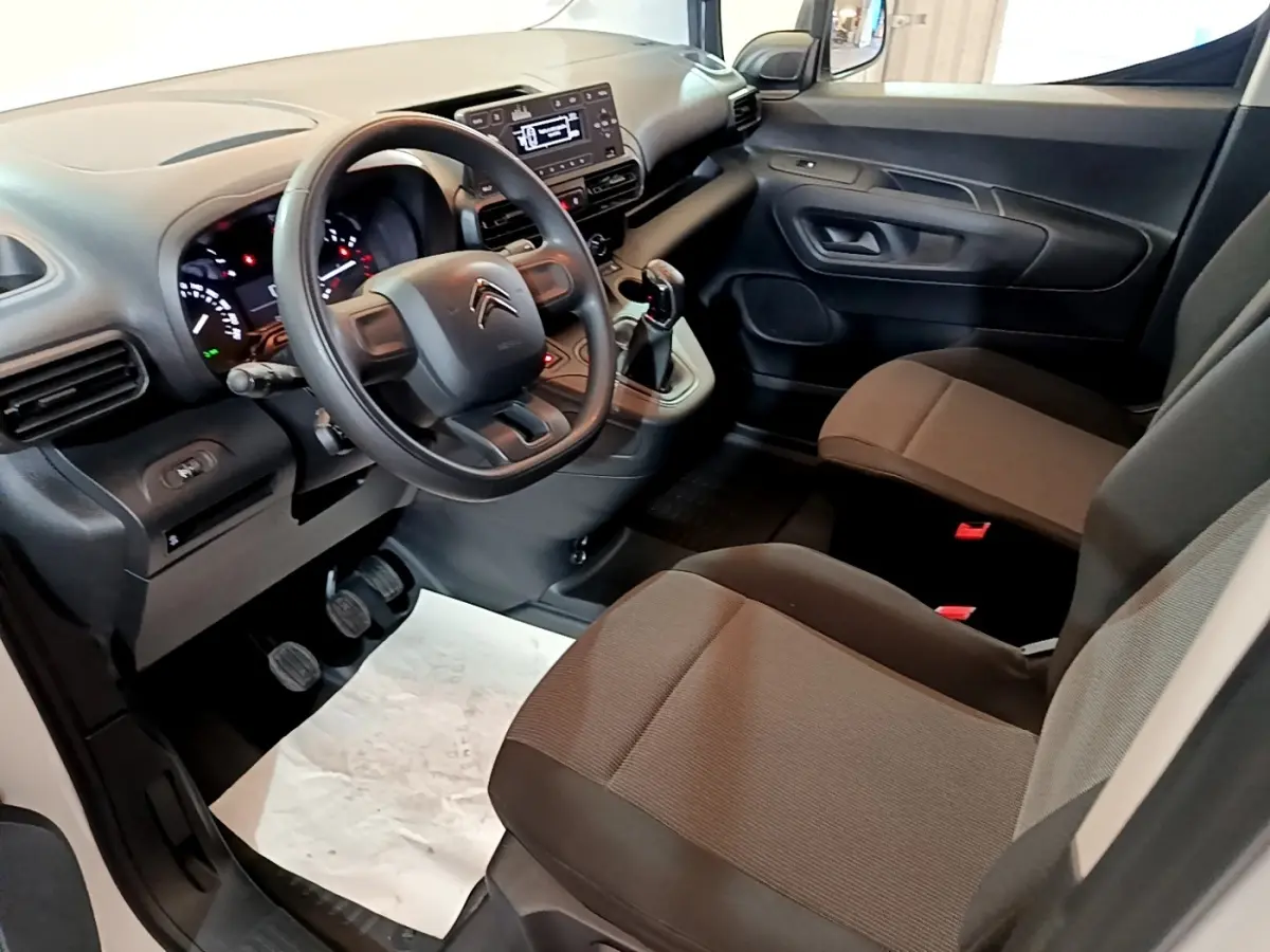 Intérieur côté conducteur du Citroën Berlingo 2021, volant, tableau de bord et sièges en tissu marron visibles.