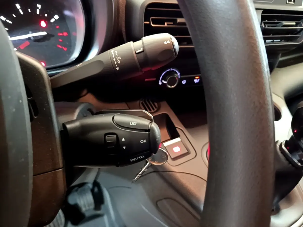 Gros plan sur le volant et commandes au volant du Citroën Berlingo blanc, avec tableau de bord et clés visibles.