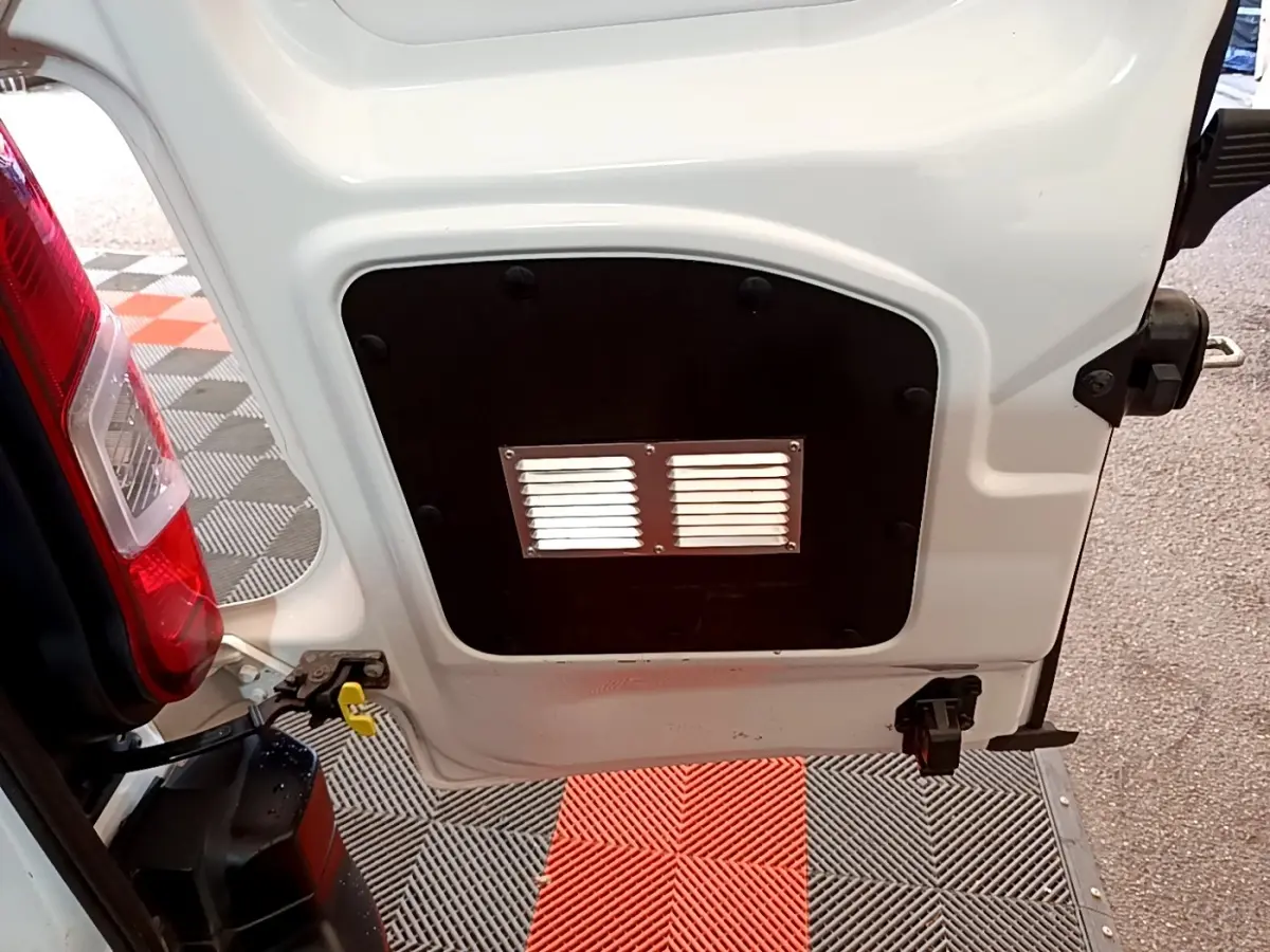 Détail de la porte arrière gauche ouverte d'un Citroën Berlingo blanc, montrant une cloison pleine avec grille d'aération.