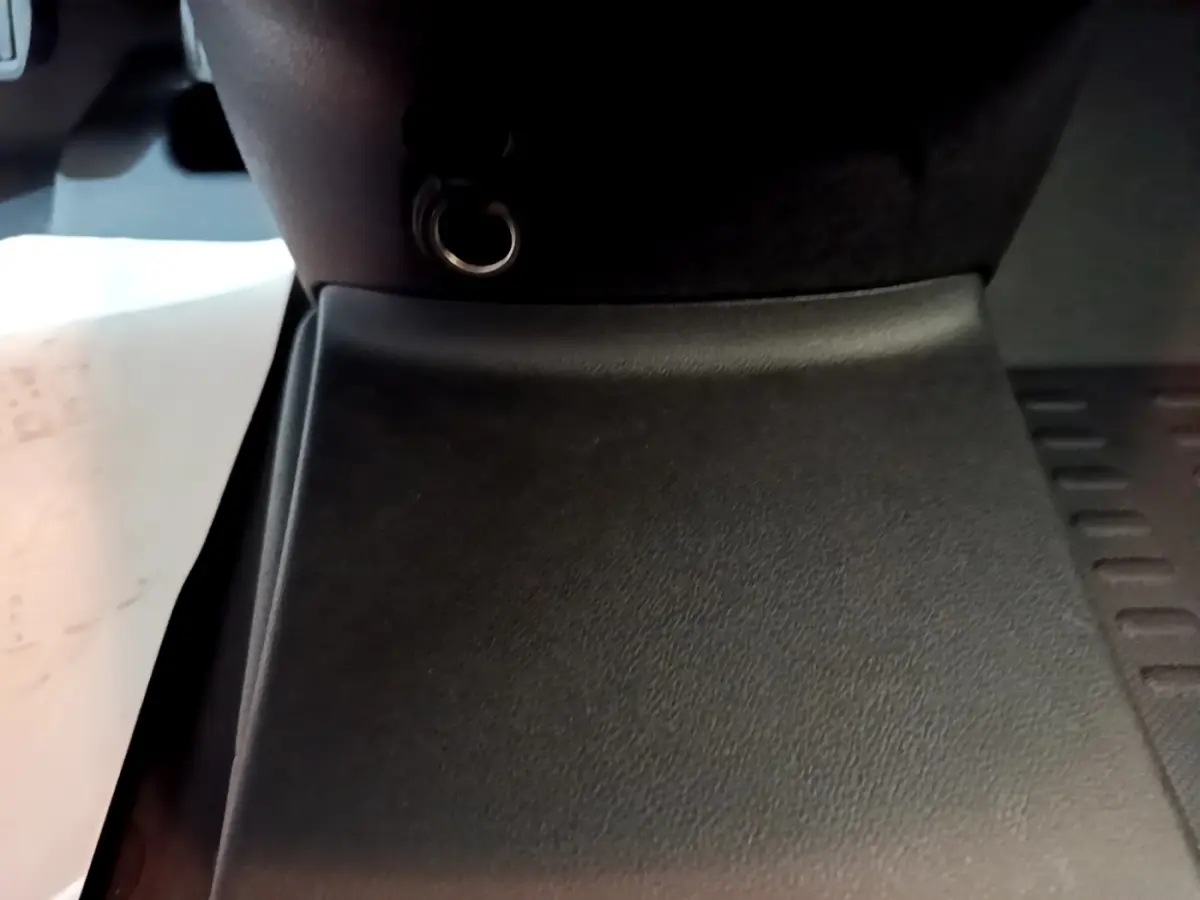 Gros plan sur la console centrale noire du Citroën Berlingo blanc, montrant une prise 12V et un tapis de sol.