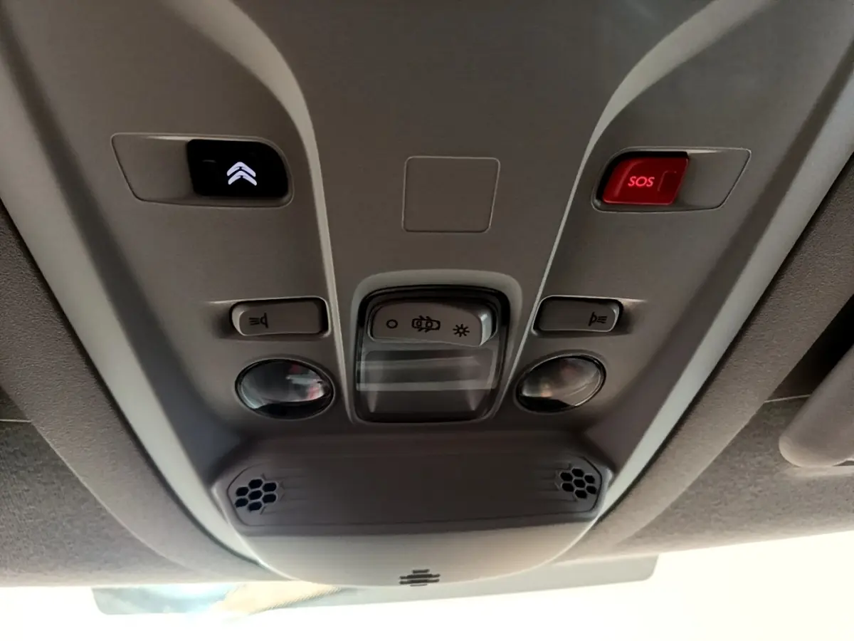Vue en contre-plongée du plafonnier gris clair du Citroën Berlingo 2021 avec boutons d'éclairage et alarme SOS rouge.