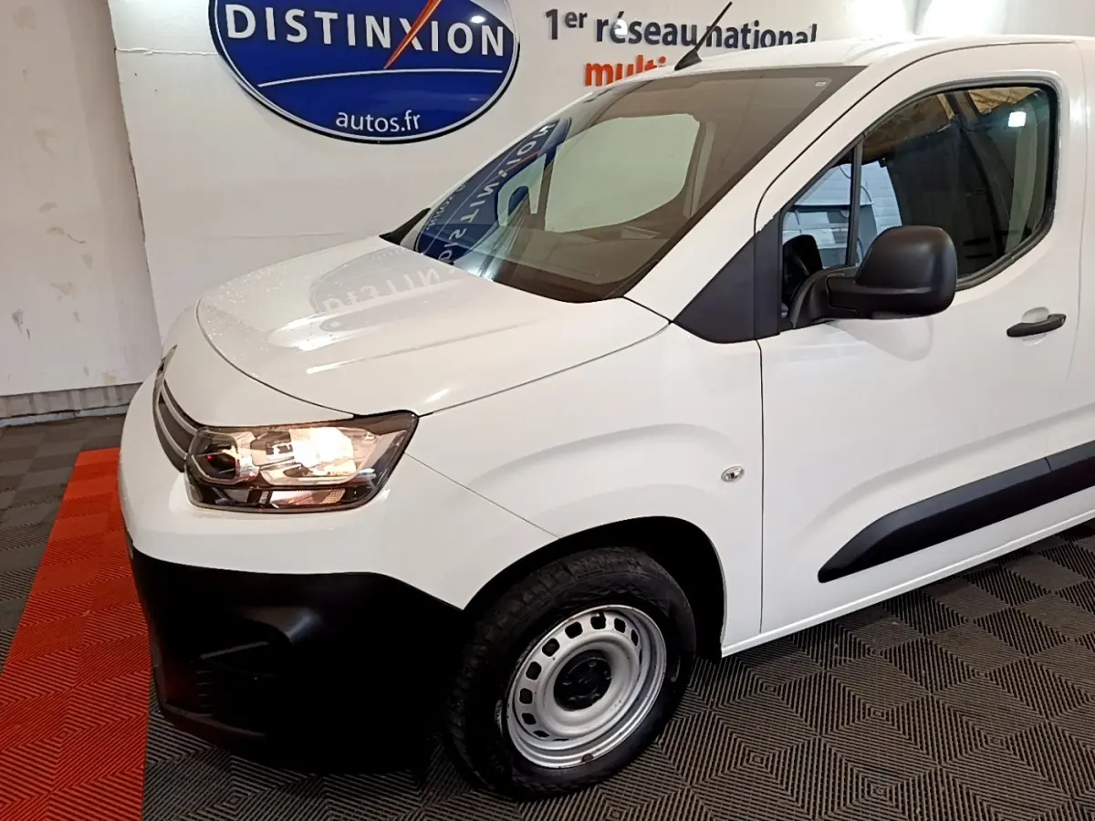 Vue 3/4 avant droit d'un Citroën Berlingo blanc avec phares allumés et jantes acier simples.