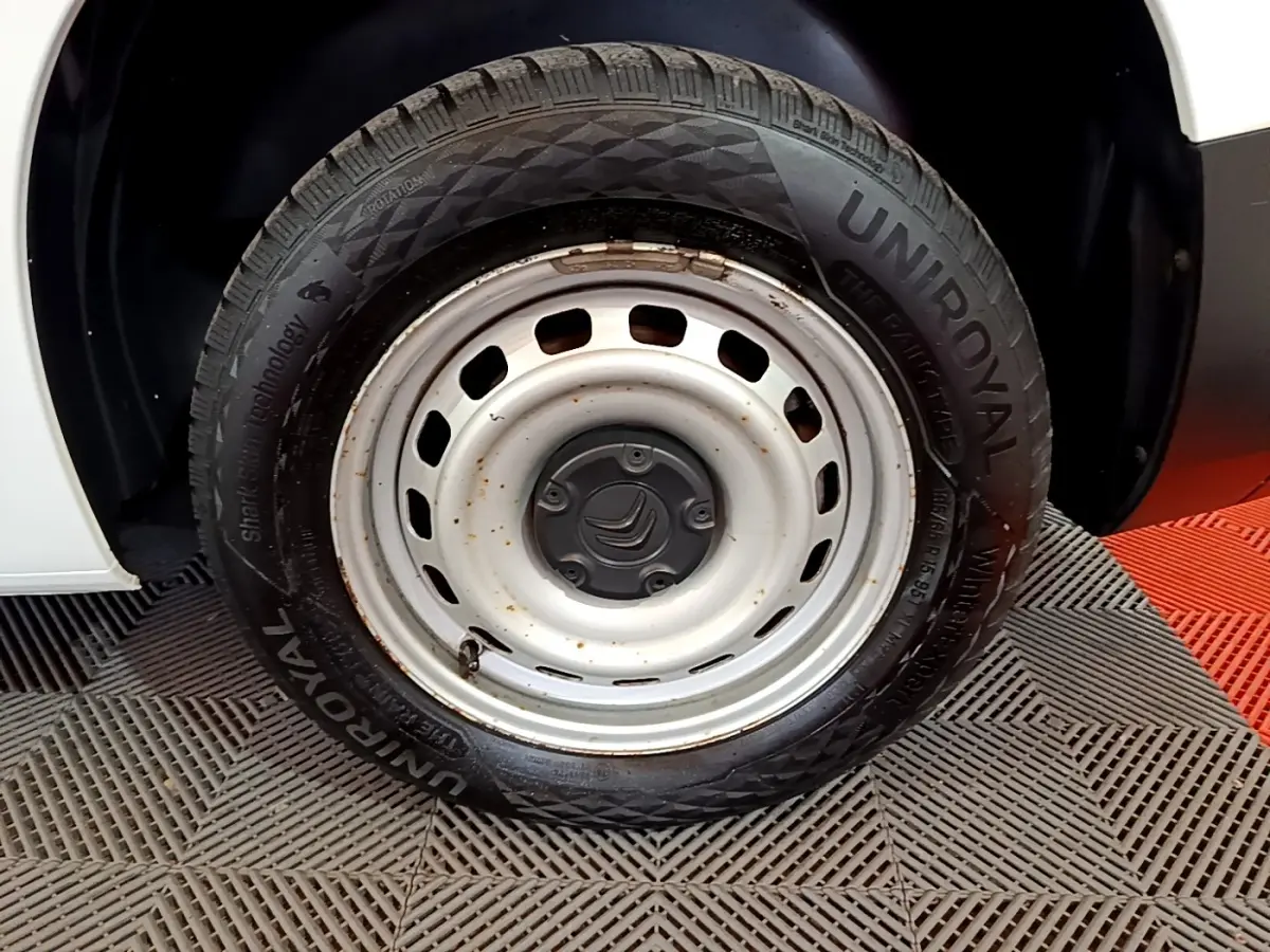 Gros plan sur la roue acier blanche et pneu Uniroyal d'un Citroën Berlingo blanc, partie arrière droite visible.