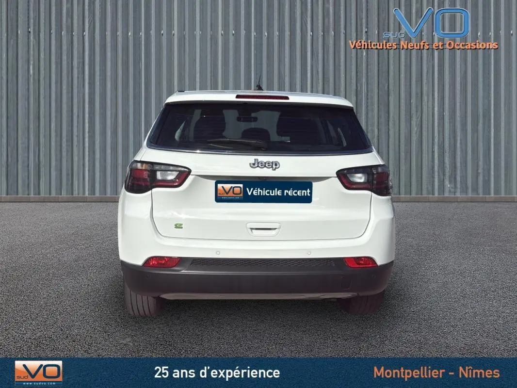 Vue arrière d'un Jeep Compass blanc 2024 avec feux LED et logo Jeep visible sur un fond industriel.
