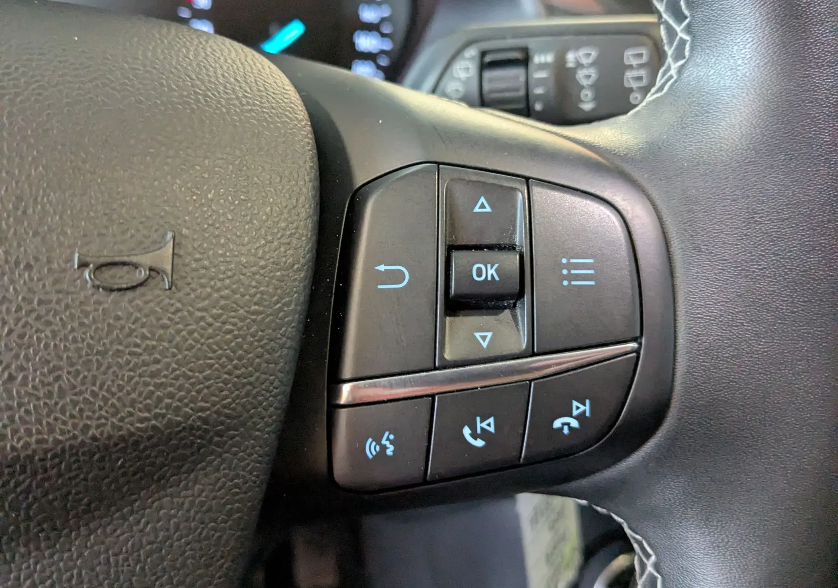 Gros plan sur les commandes multifonctions noires à droite du volant du Ford Puma gris 2020, avec boutons de navigation et appel.