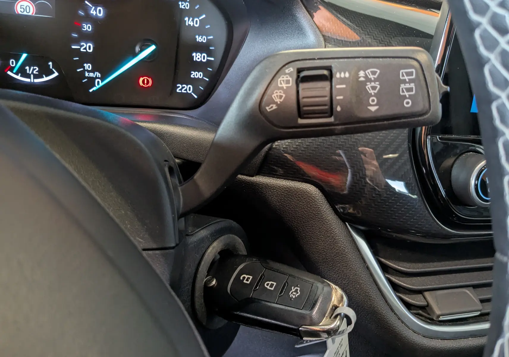 Gros plan sur la colonne de direction et le tableau de bord du Ford Puma gris, avec clé insérée et commandes d’essuie-glace visibles.