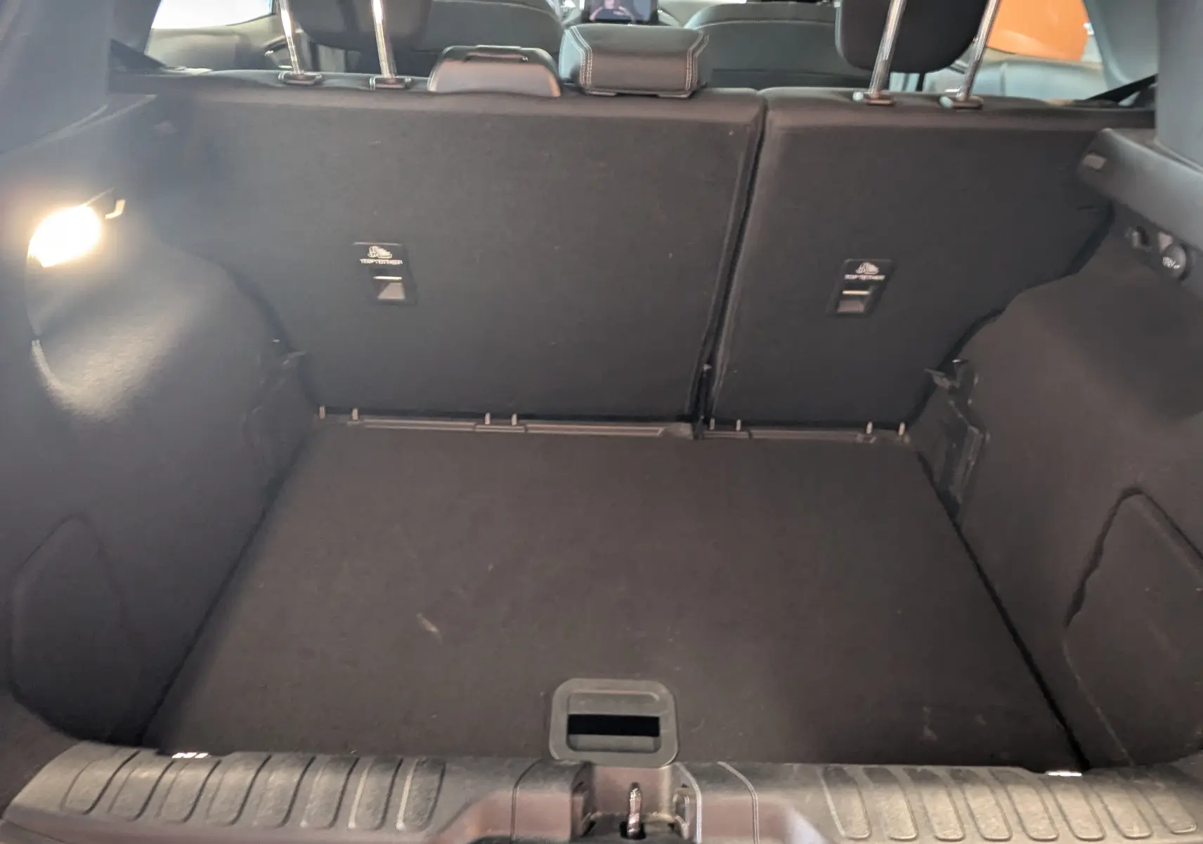 Coffre ouvert de la Ford Puma gris, vue intérieure arrière montrant le tapis de coffre et les dossiers de sièges rabattus.