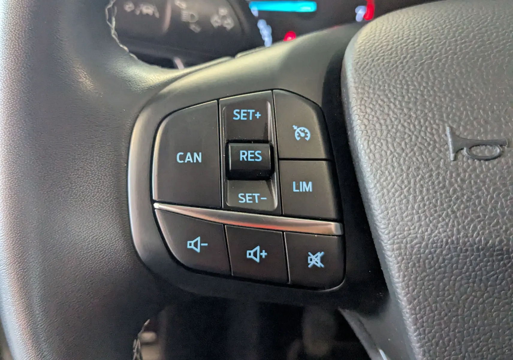 Gros plan sur les commandes de régulateur de vitesse et volume au volant noir du Ford Puma gris 2020.