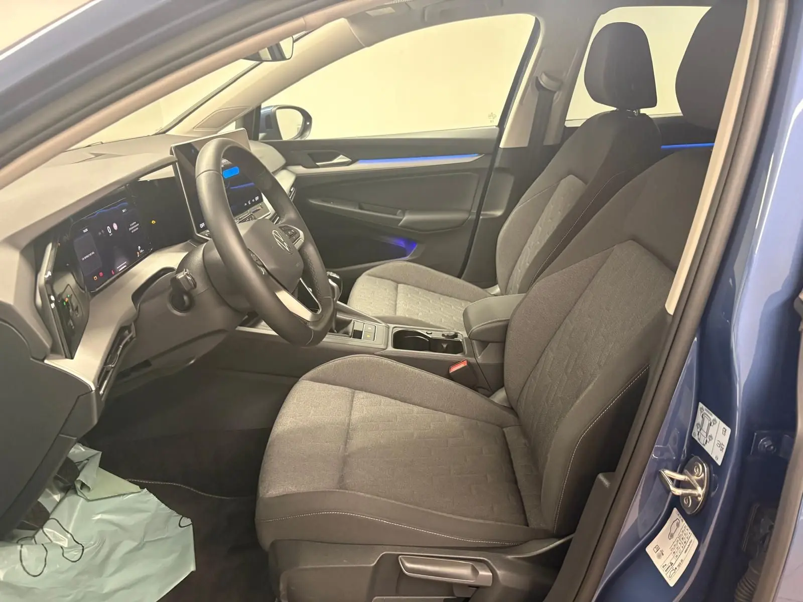 Vue intérieure côté conducteur de la Volkswagen Golf 1.5 TSI 116 BVM6 Bleu Anémone avec sièges tissu gris et éclairage d'ambiance bleu.