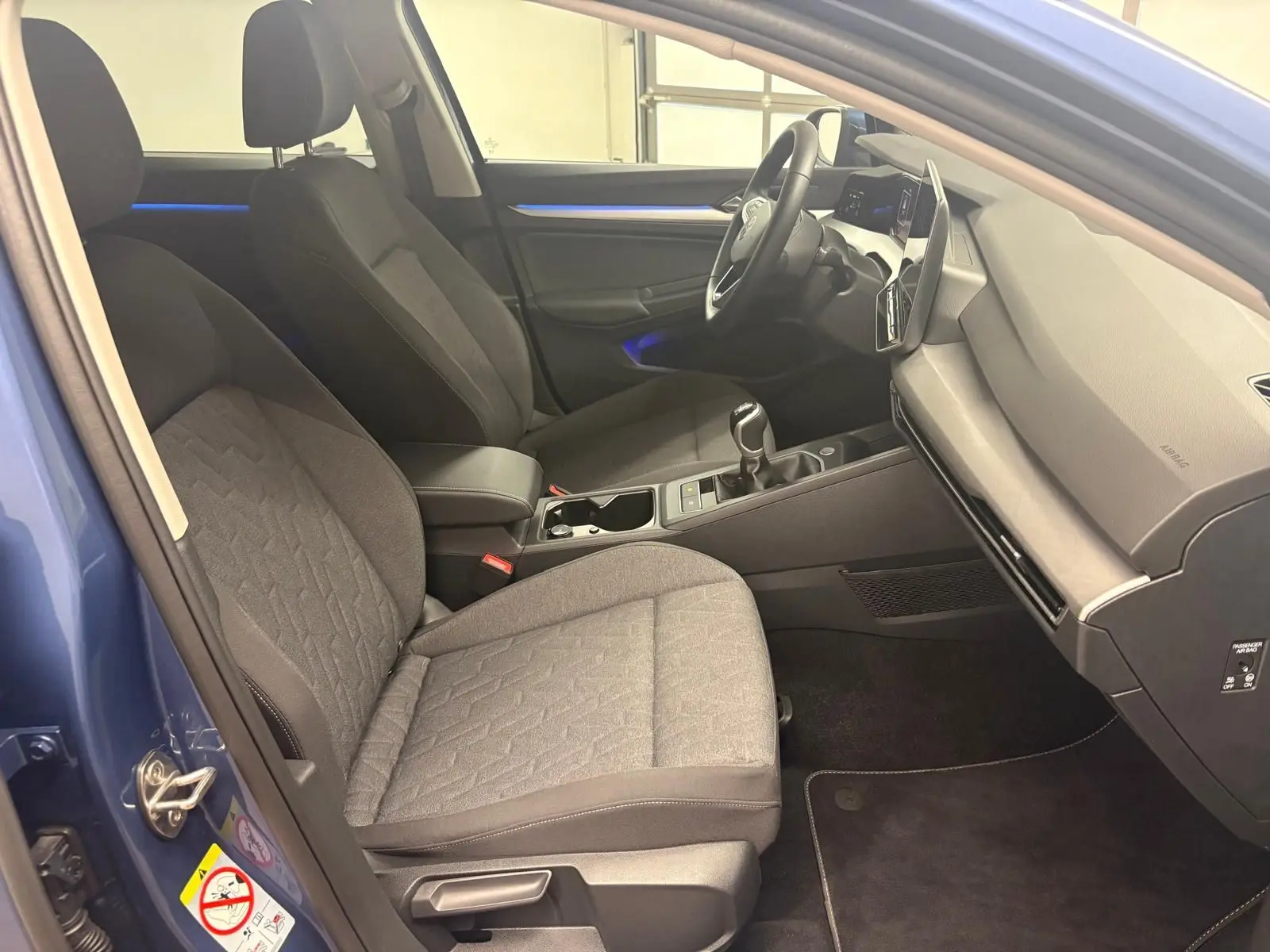 Vue intérieure côté conducteur de la Volkswagen Golf 1.5 TSI Bleu Anémone avec sièges tissu gris et éclairage d'ambiance bleu.