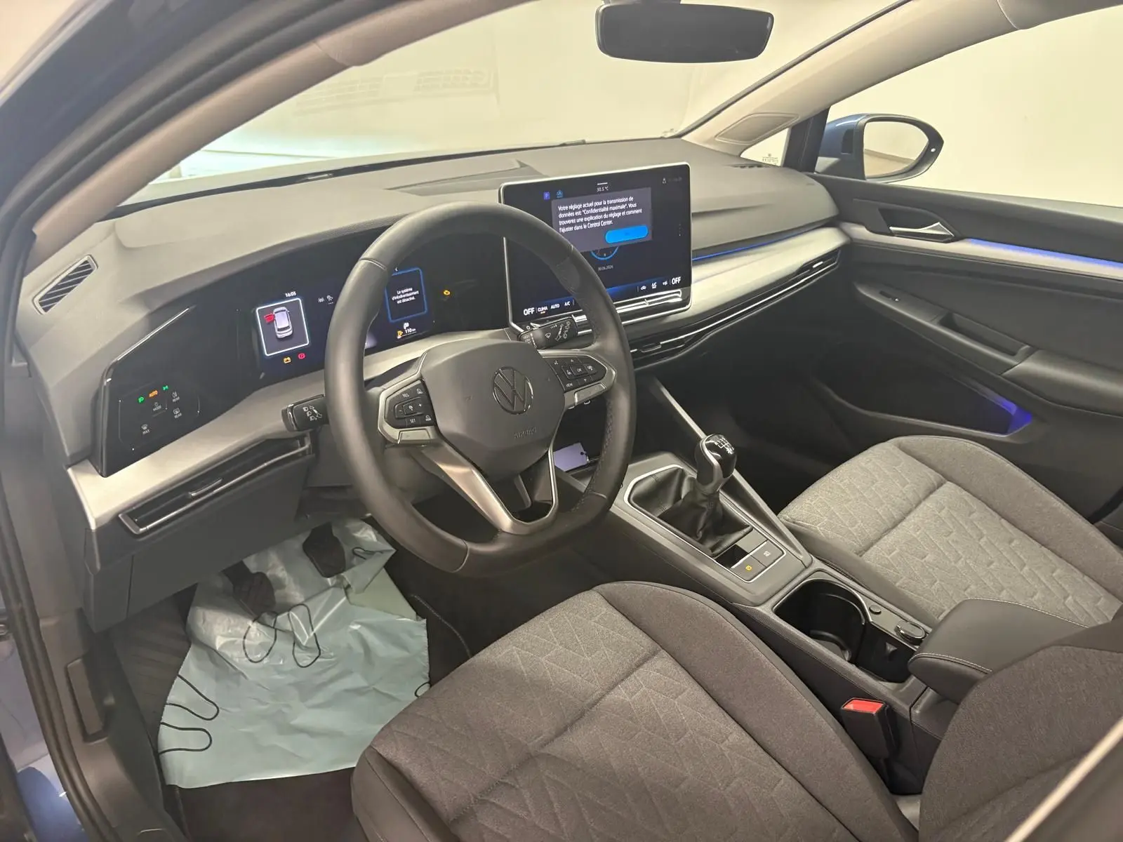 Vue intérieure côté conducteur de la Volkswagen Golf 1.5 TSI 116 BVM6 VW Edition avec tableau de bord numérique et sellerie grise.