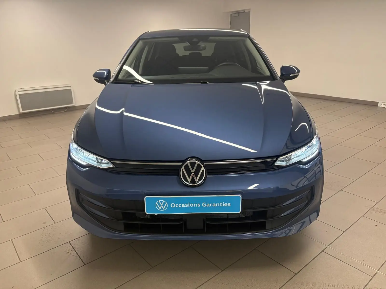 Volkswagen Golf 1.5 TSI bleu Anémone vue de face, avec phares allumés et calandre noire brillante.
