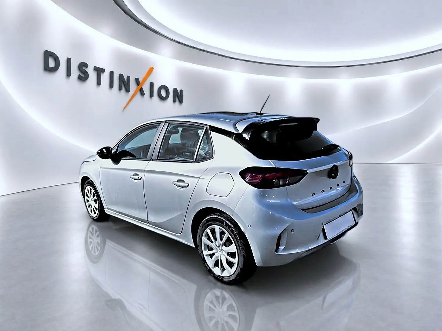 Vue 3/4 arrière droite de l'Opel Corsa 2025 gris alu avec becquet noir et feux arrière foncés dans un showroom lumineux.