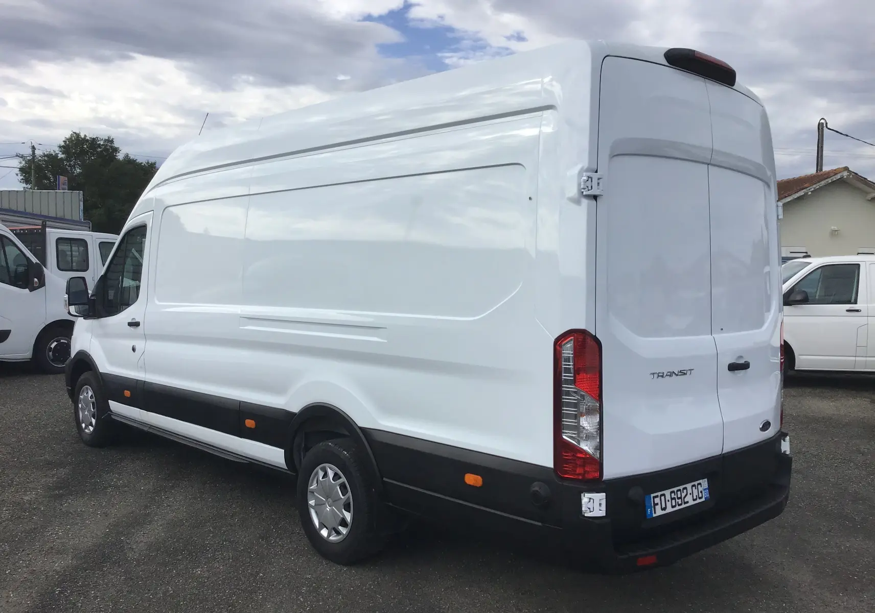 Vue 3/4 arrière droite d'un fourgon Ford Transit blanc avec toit surélevé et feux arrière verticaux.