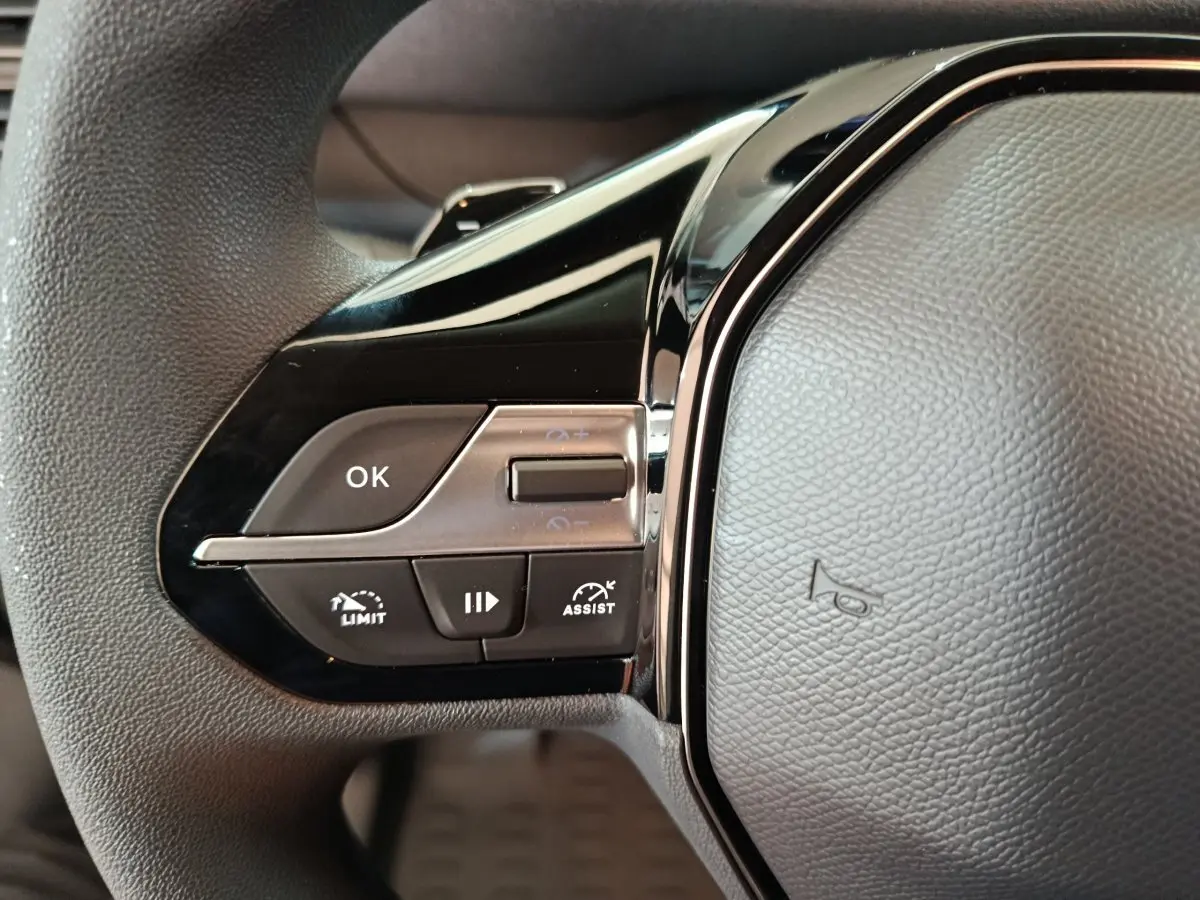 Gros plan sur les commandes gauche du volant noir du Peugeot Partner XL blanc 2025 avec boutons multifonctions.