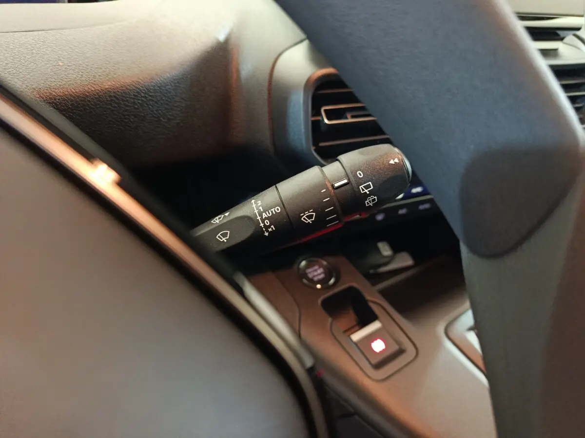 Gros plan sur la manette d'essuie-glace à gauche du volant dans l'habitacle sombre du Peugeot Partner blanc 2025.