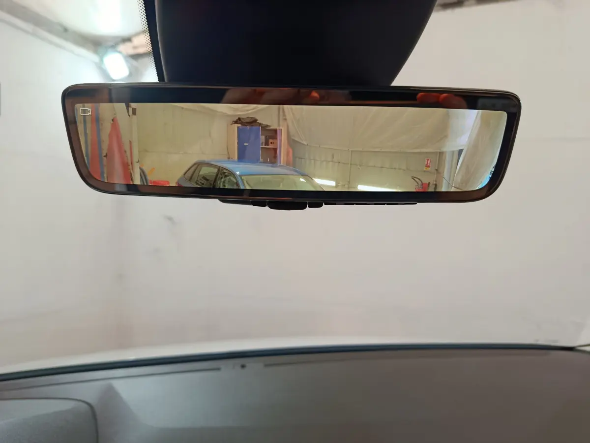 Rétroviseur intérieur affichant en reflet une voiture bleue vue de trois quarts arrière dans un garage.