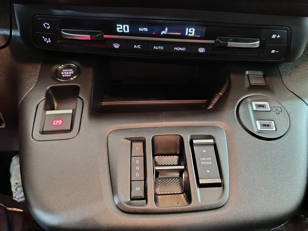 Vue rapprochée de la console centrale noire du Peugeot Partner 2025 avec commandes de climatisation et boîte automatique.