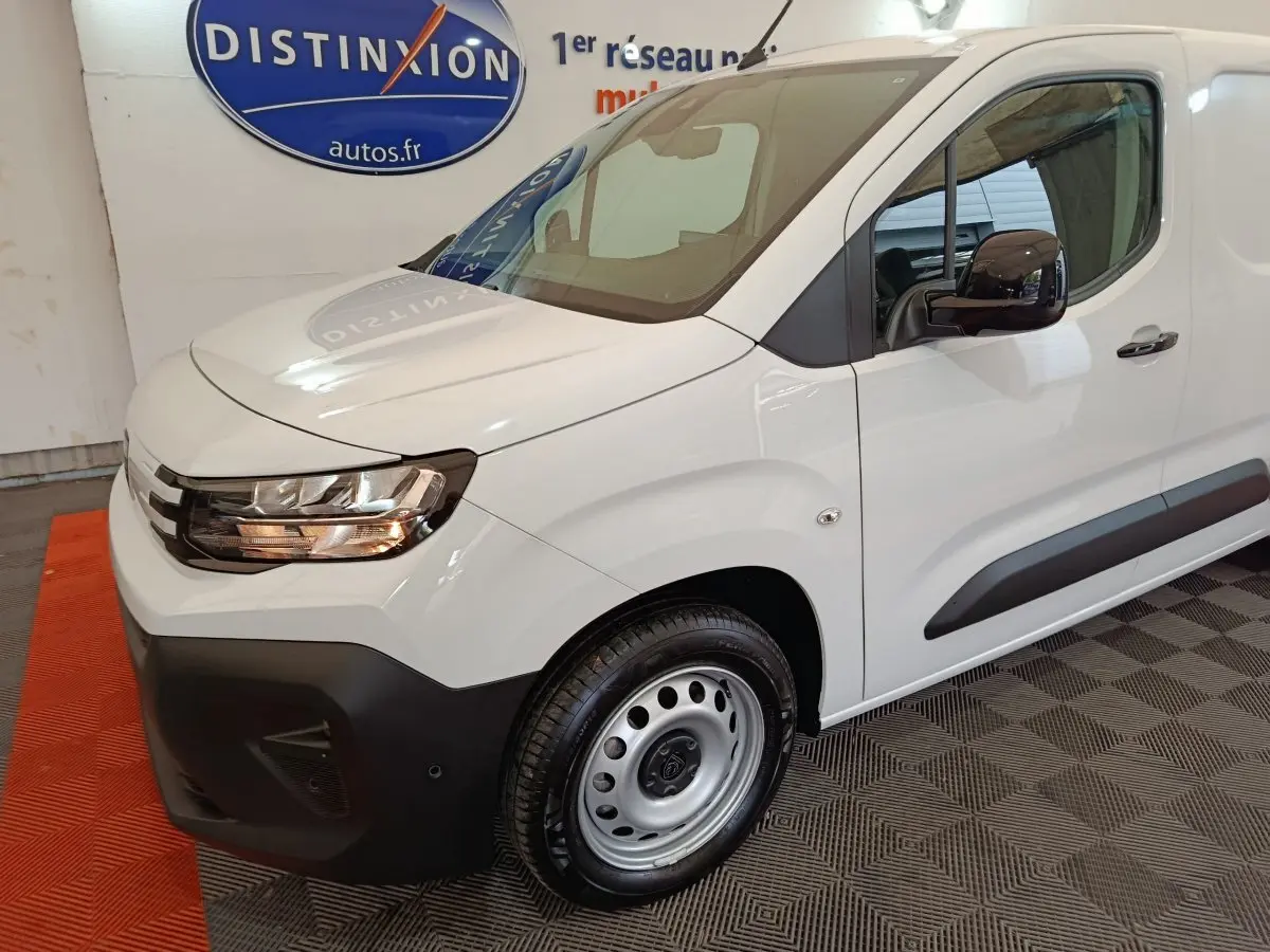 Vue 3/4 avant droit d'un Peugeot Partner XL blanc avec phares halogènes et jantes acier en intérieur showroom.