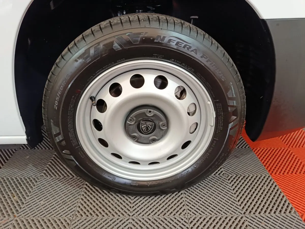 Gros plan sur la roue avant droite d'un Peugeot Partner blanc avec jante acier et logo Peugeot central.