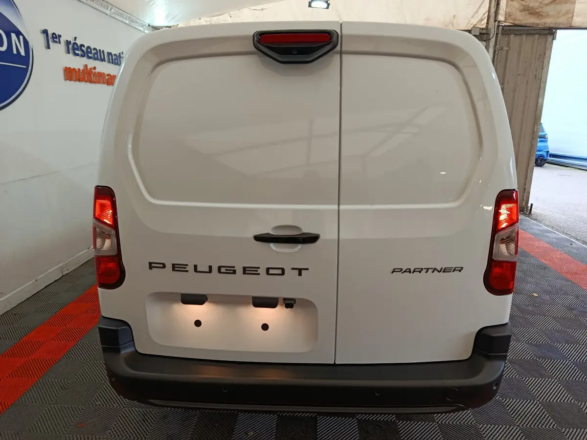 Vue arrière du Peugeot Partner blanc 2025 avec portes battantes et feux arrière allumés dans un garage.
