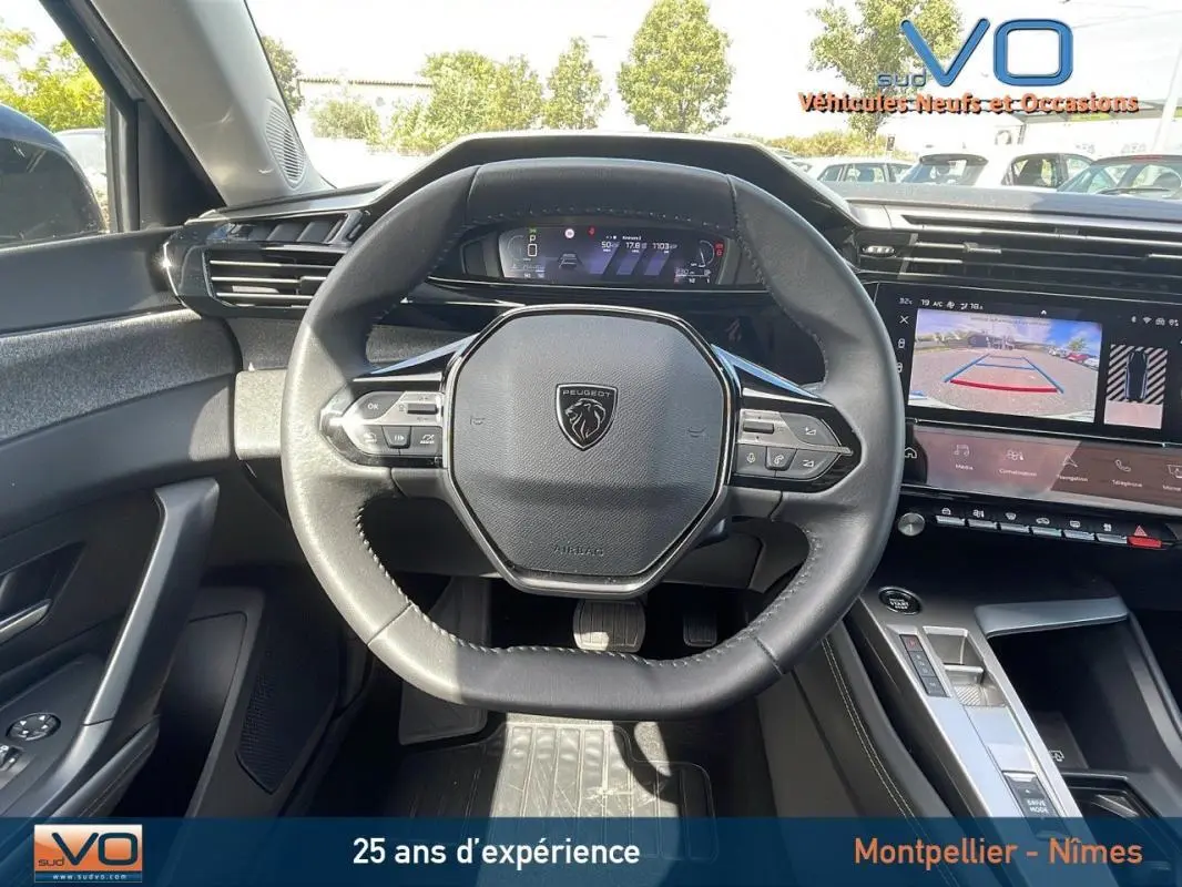 Vue intérieure centrée sur le volant noir de la Peugeot 308 gris, avec tableau de bord numérique et écran tactile affichant la caméra de recul.