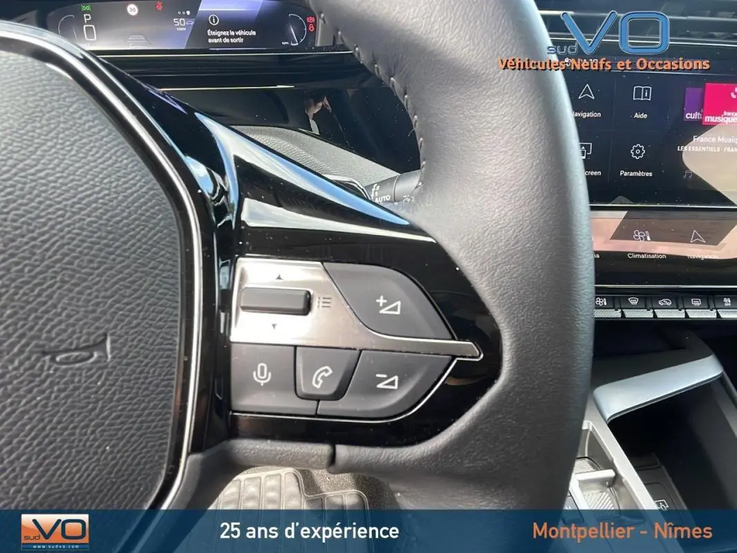 Gros plan sur les commandes au volant gauche d'une Peugeot 308 gris, avec affichage numérique et écran tactile visible.