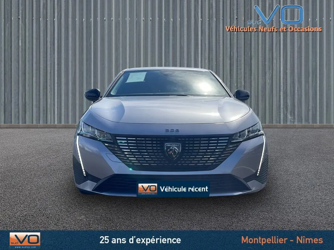 Vue frontale d’une Peugeot 308 gris métallisé 2024 avec calandre distinctive et feux LED verticaux allumés.